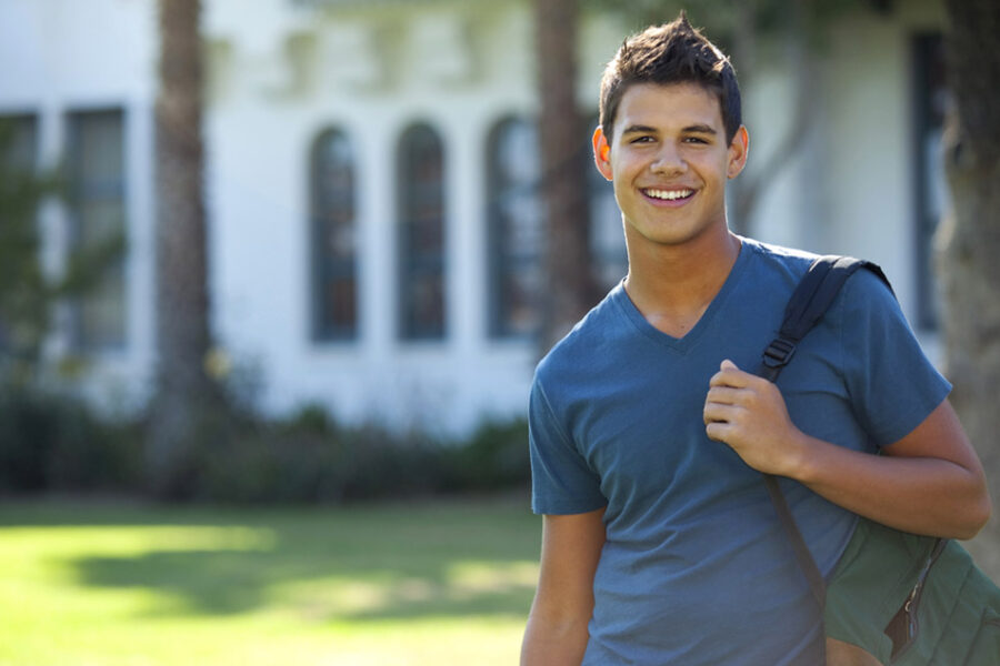 College student smiling in front of university building, investing in education.
