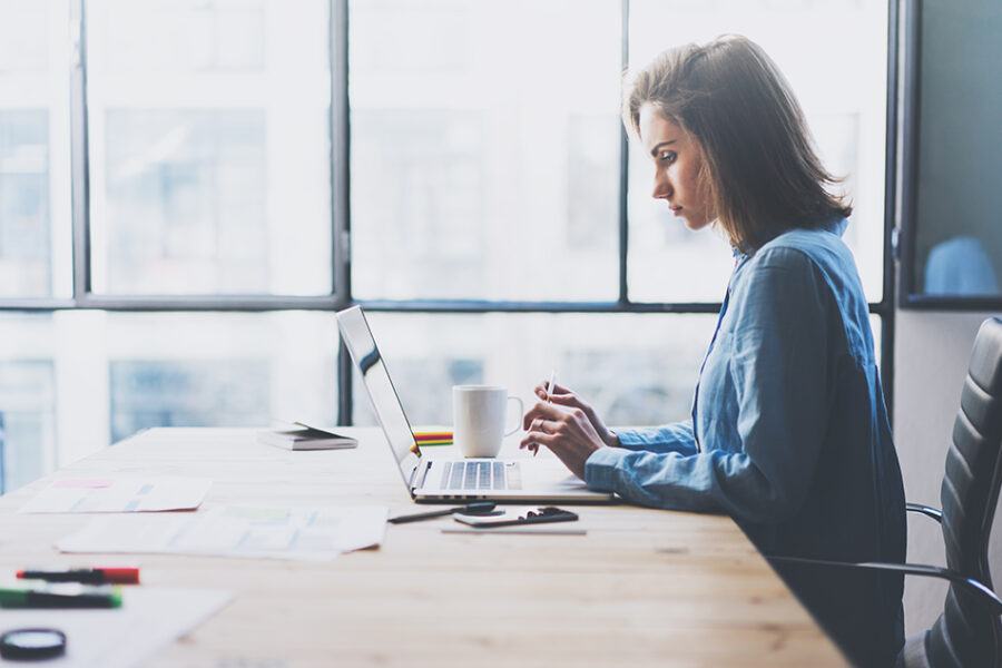 Photo of business woman sitting at desk with researching on laptop.