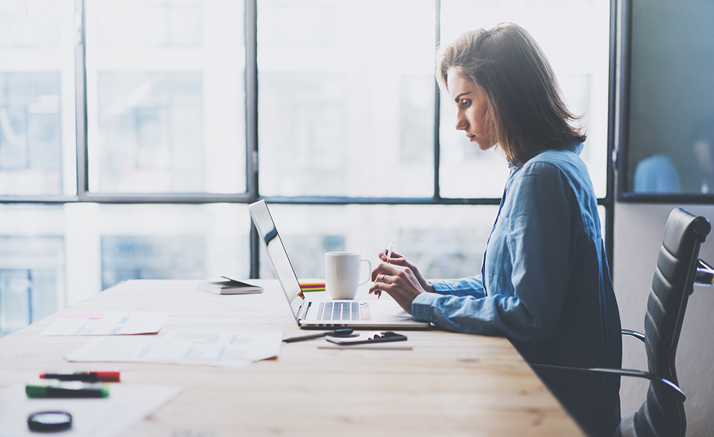 Photo of business woman sitting at desk with researching on laptop.