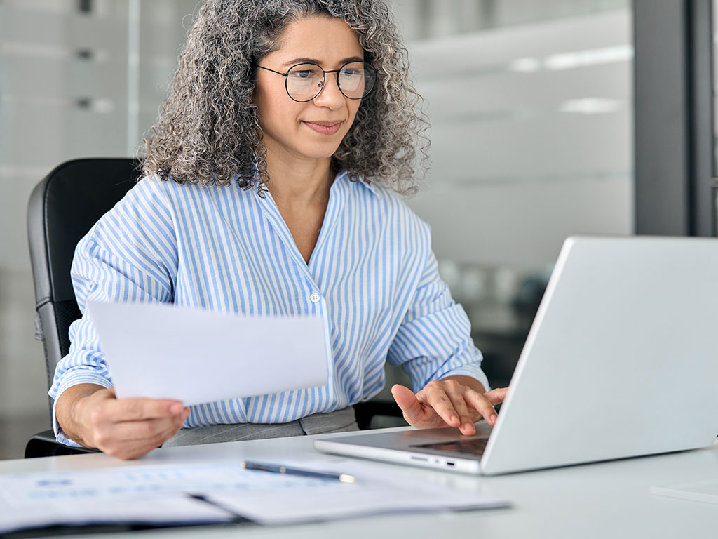 Mature Professional Woman At Desk Computer using postive pay system