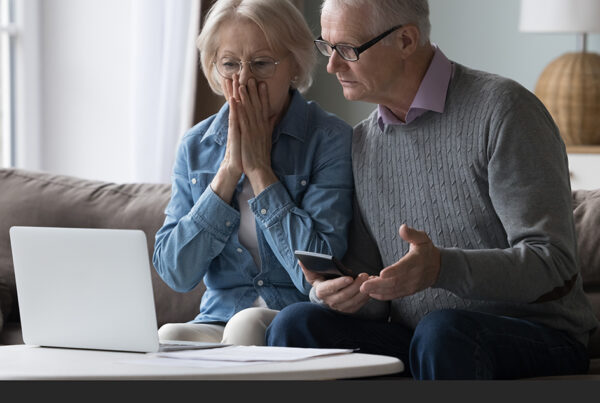 Couple at computer with mobile phone looking shocked