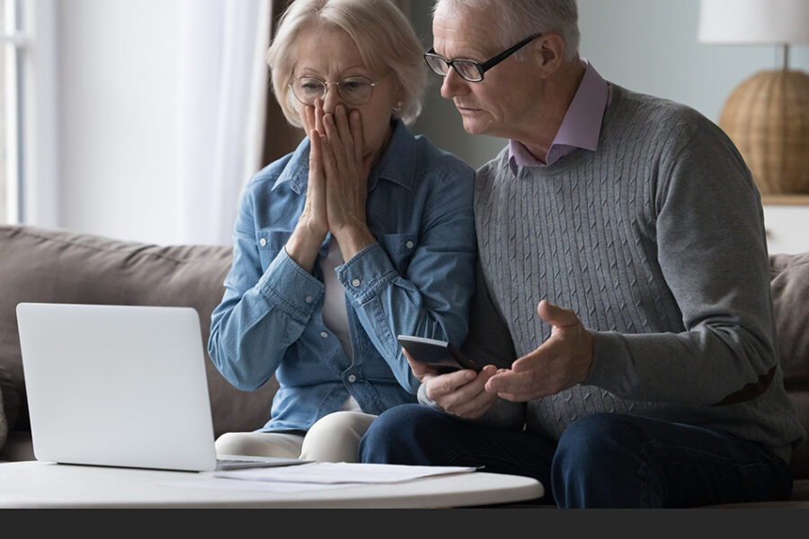 Couple at computer with mobile phone looking shocked