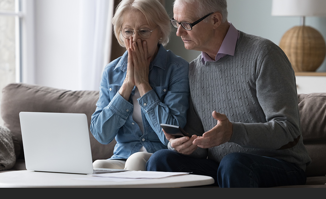 Couple at computer with mobile phone looking shocked