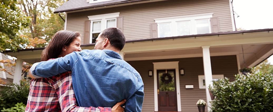 Couple embracing in front of a home, illustrating the home buying process with Bank Midwest.